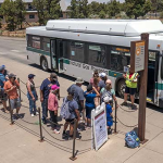 Visitors waiting beside a white and green Grand Canyon National Park shuttle bus