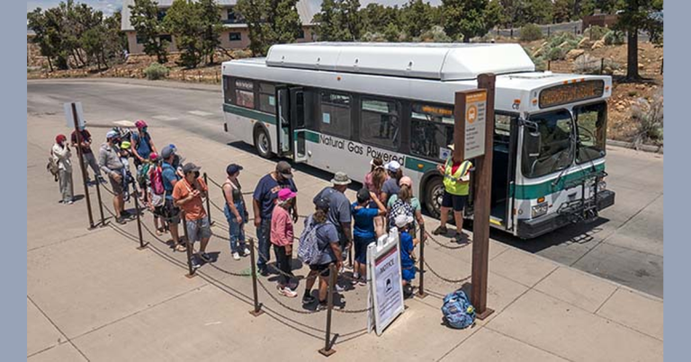 Visitors waiting beside a white and green Grand Canyon National Park shuttle bus